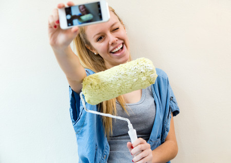 Portrait of young beautiful woman painting her new home. Selfie concept.