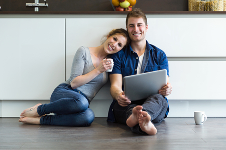 Portrait of beautiful young couple using they digital tablet in the kitchen at home.の写真素材