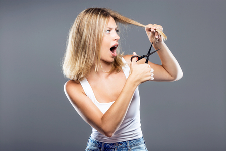 Portrait of beautiful young woman cutting her hair over gray background.の写真素材