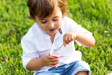 Portrait of the little boy eating yogurt in the park.の写真素材