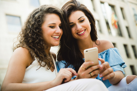 Portrait of beautiful young women having fun with smartphones in the street.の写真素材