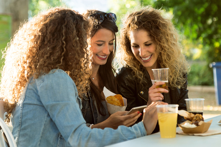 Portrait of three beautiful young women using they mobile phone in the street.の写真素材