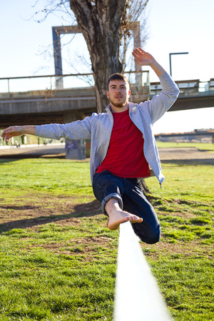 Portrait of handsome young man walking on slackline in the park.