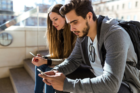 Portrait of beautiful young couple using mobile phone in the street.