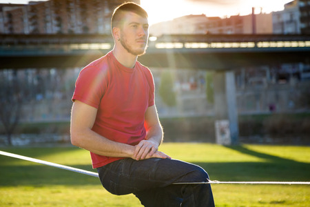 Portrait of handsome young man thinking on slackline in the park.