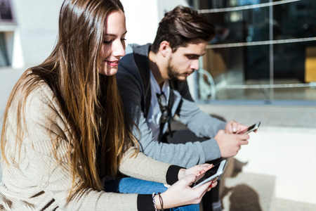 Portrait of beautiful young couple using mobile phone in the street.