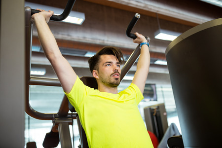 Portrait of handsome young man doing muscular exercise in gym.