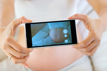 Portrait of pregnant woman taking a photo of her belly.の写真素材