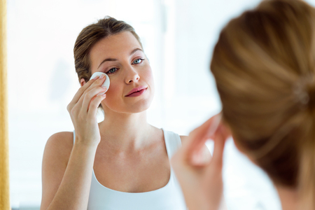 Portrait of beautiful young woman is cleaning her face while looking in the mirror in the bathroom.の写真素材