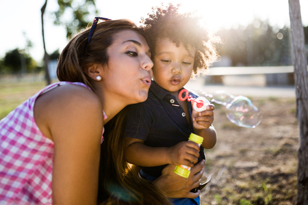 Portrait of beautiful young mother with her son blowing soap bubbles in the park.の写真素材