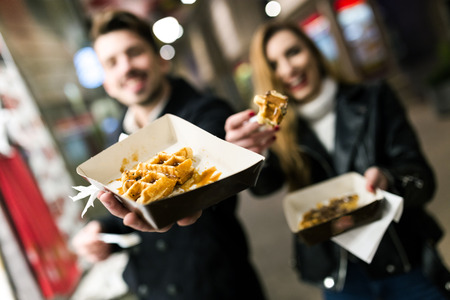Portrait of beautiful young couple eating waffles in the street.