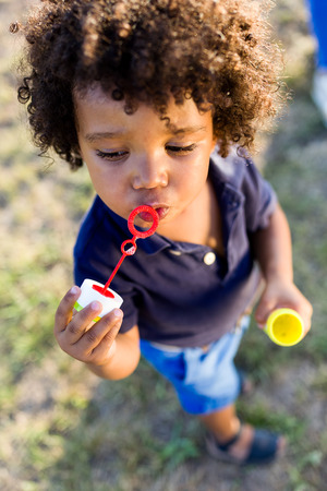 Portrait of a african american baby blowing soap bubbles in the park.