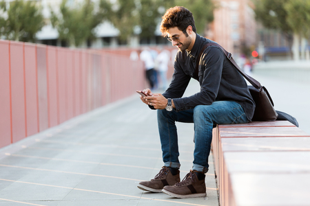 Portrait of modern young man using his mobile phone in the street.の写真素材
