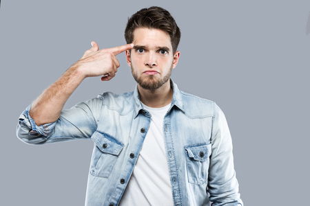 Portrait of handsome young man making a shooting gesture at her head over gray background.の写真素材