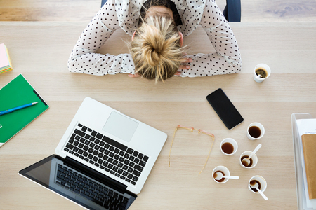 Shot of tired young businesswoman sleeping on her desk in the office.の写真素材