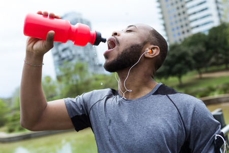 Portrait of fit and sporty young man drinking water in the city.の写真素材