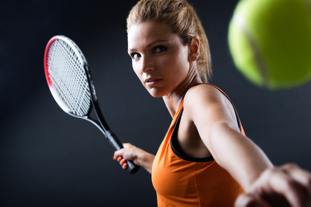 Portrait of beautiful woman playing tennis indoor. Isolated on black.の写真素材