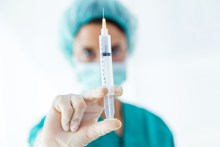 Portrait of confident female medical worker wearing hat and mask posing with a syringe in his hand and looking to the camera.の写真素材