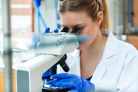 Portrait of young woman looking through microscope in laboratory.