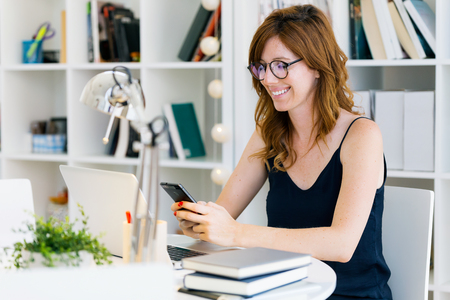Portrait of beautiful young woman working with her mobile phone at home.の写真素材