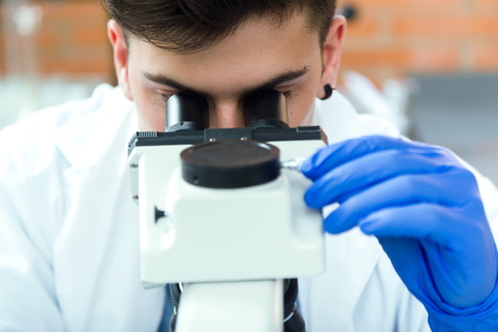 Portrait of young man looking through microscope in laboratory.の写真素材