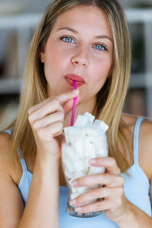 Portrait of beautiful young woman looking at camera while simulating to drink sugar in a glass cup at home.の写真素材
