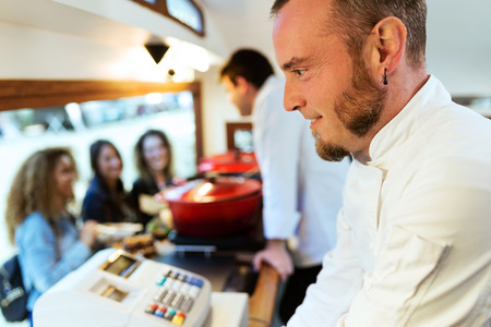 Close-up of a chef smiling in a food truck. In the background, other chef talking to three clients.