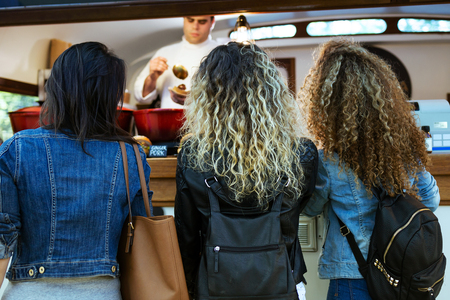 Portrait of three beautiful young women buying meatballs on a food truck in the park.