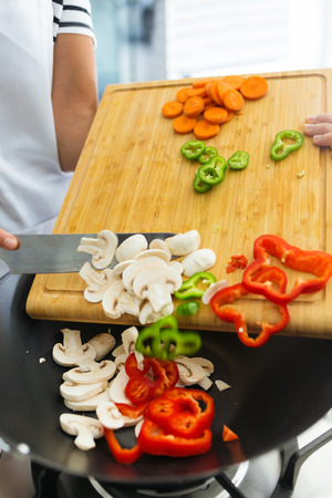 Close-up of hands of healthy woman putting fresh vegetables in the pan in the kitchen at home.の写真素材