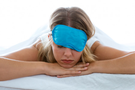 Shot of beautiful young exhausted woman with sleep mask suffering insomnia trying to sleep over white blackground.の写真素材