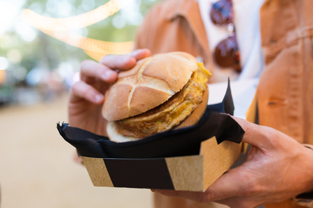 Close-up of hands of young fashion man visiting eat market and holding hamburger in the street.の写真素材