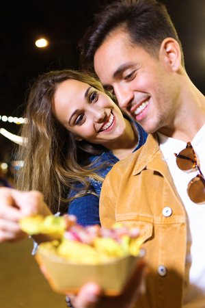Shot of lovely attractive couple eating potatoes together in eat market in the street.の写真素材