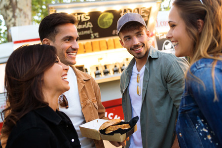 Shot of group of attractive young friends talking while visiting eat market in the street.