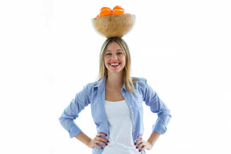 Portrait of pretty young woman holding a bowl over her head with oranges over white background.の写真素材