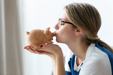 Shot of pretty young woman kissing her piggy bank at home.の写真素材