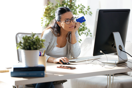 Shot of pretty young woman holding blue credit card for shopping online with computer at home.の写真素材