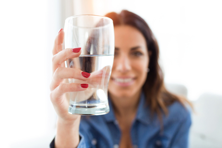 Portrait of pretty young woman smiling while looking at the camera through the glass of water at home.の写真素材