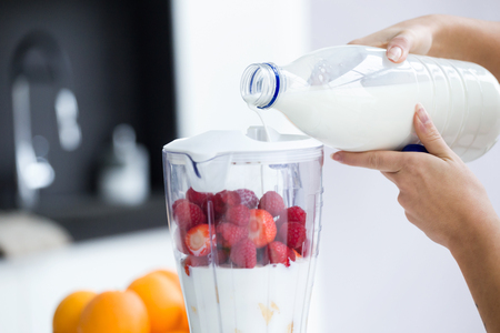 Close-up of woman's hands while she filling the milk blender to prepare a smoothie in the kitchen.の写真素材