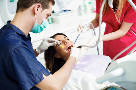 Shot of concentrate dentist and his assistant drilling tooth to female patient on dental chair in dental clinic.の写真素材