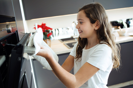 Shot of cute girl baking chocolate muffins in the oven with her family in the kitchen at home.の写真素材
