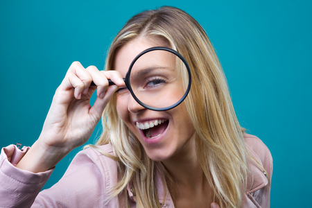 Portrait of cheerful pretty girl looking through magnifying glass isolated over blue background.の写真素材