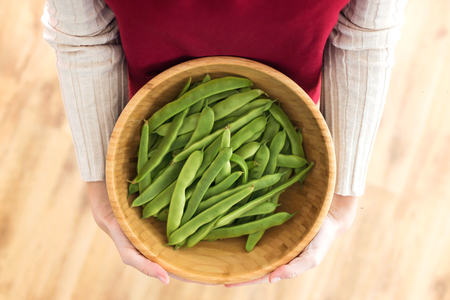 Female hands holding green beans in round wooden bowl at home.の写真素材