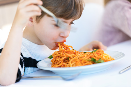 Shot of hungry little boy eating spaghetti with tomato sauce in the kitchen at home.の写真素材