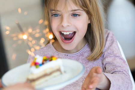 Shot of funny little girl surprised and having fun with birthday cake in the kitchen at home.の写真素材