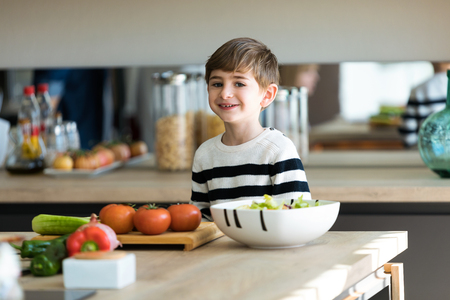 Shot of little cute boy preparing salad while looking at the camera in the kitchen at home.の写真素材