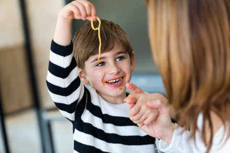 Shot of cute little boy having fun with his young mother while eating spaghetti on kitchen at home.の写真素材