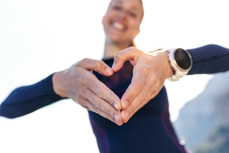 Shot of sporty young woman making heart shape with hands while posing to camera on mountain.の写真素材