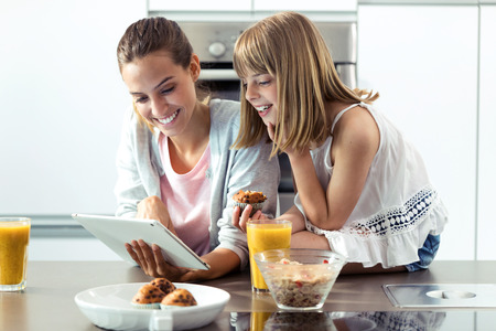 Shot of pretty young mother and her daughter using digital tablet while having breakfast at home.の写真素材