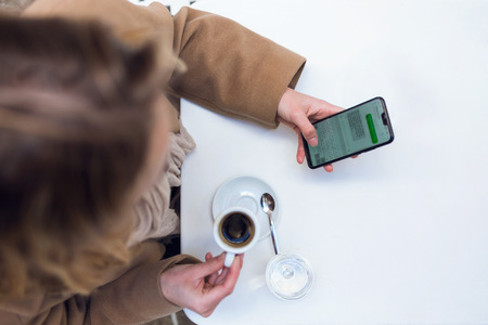 Shot of pretty young woman using her mobile phone while drinking cup of coffee in the terrace of a coffee shop.の写真素材