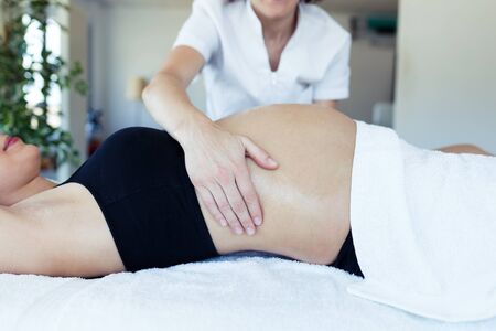 Close-up of female physiotherapist massaging tummy on pregnant woman in spa center.の写真素材